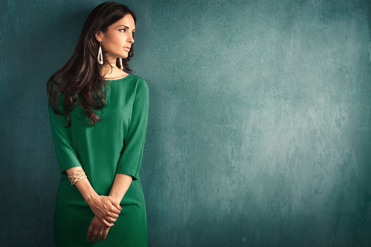 mid-shot of woman in green dress with large gold earrings on green background