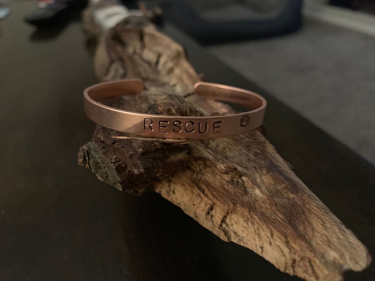 Copper cuff bracelet displayed on a log with the word rescue hand-stamped on the surface