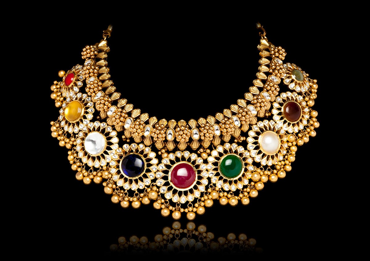 close up of ornate yellow gold necklace with various colored gemstones
