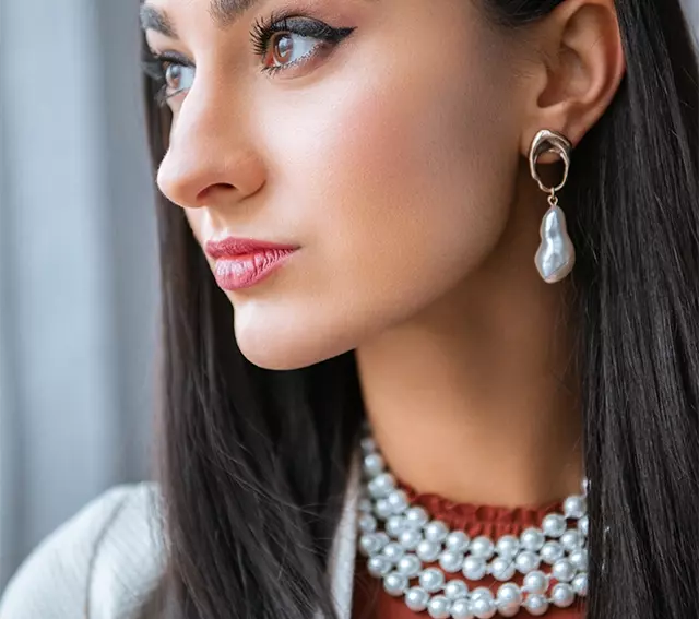 Woman wearing modern baroque pearl earrings and a four-strand pearl necklace