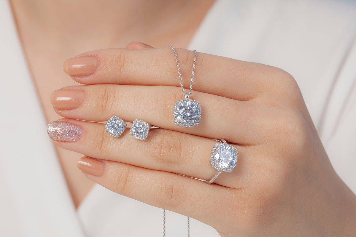 Closeup of woman’s hand holding diamond earrings, necklace, and ring
