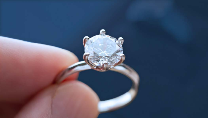 A person holding a round stone engagement ring.