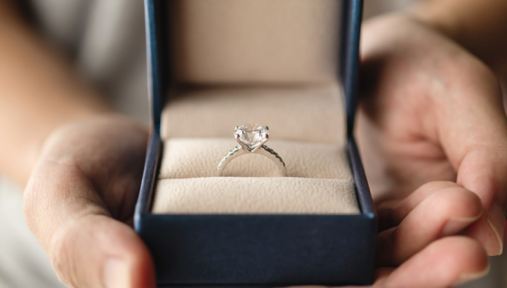 A person holds a box containing a diamond engagement ring.