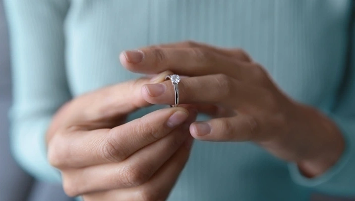 A person takes an engagement ring off their finger.